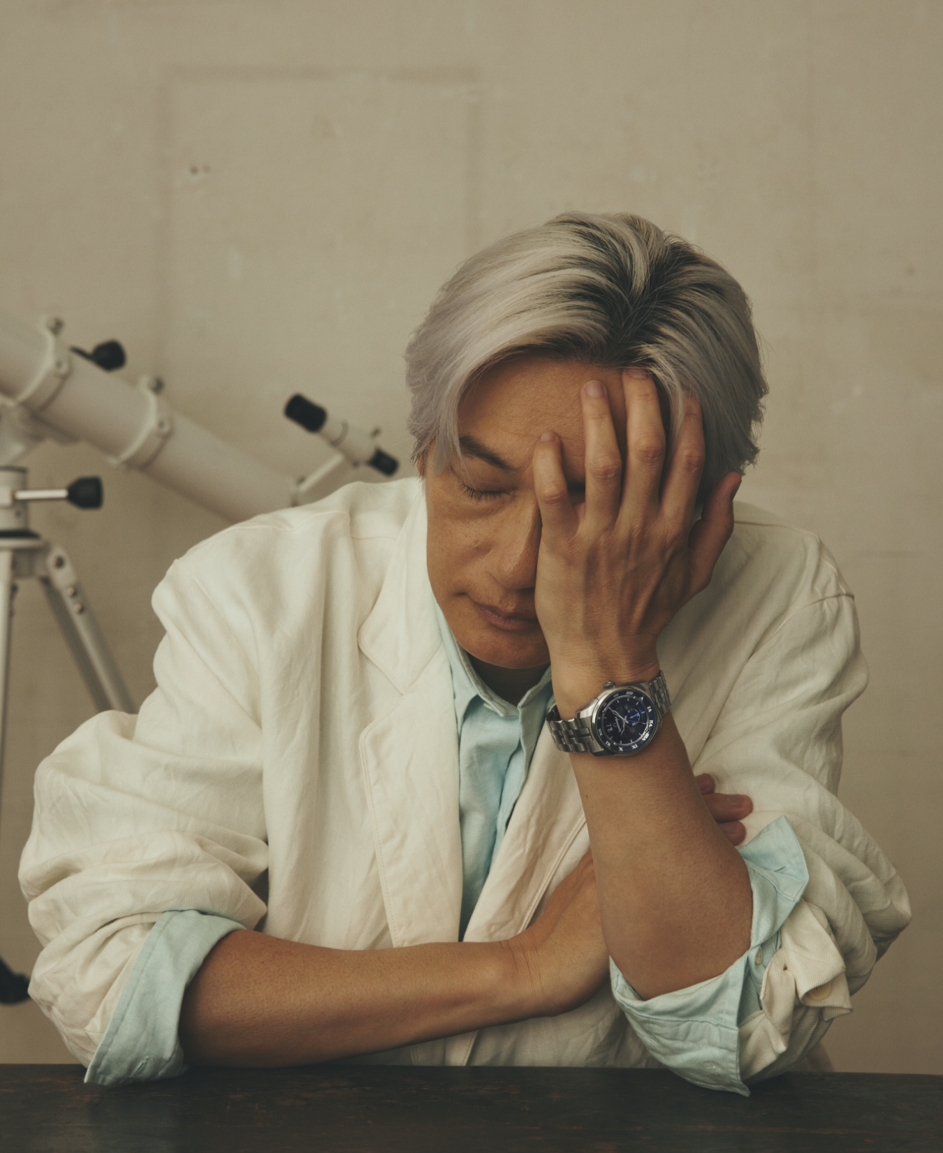 腕時計を身に着けた左手で顔をおさえている井浦新の写真