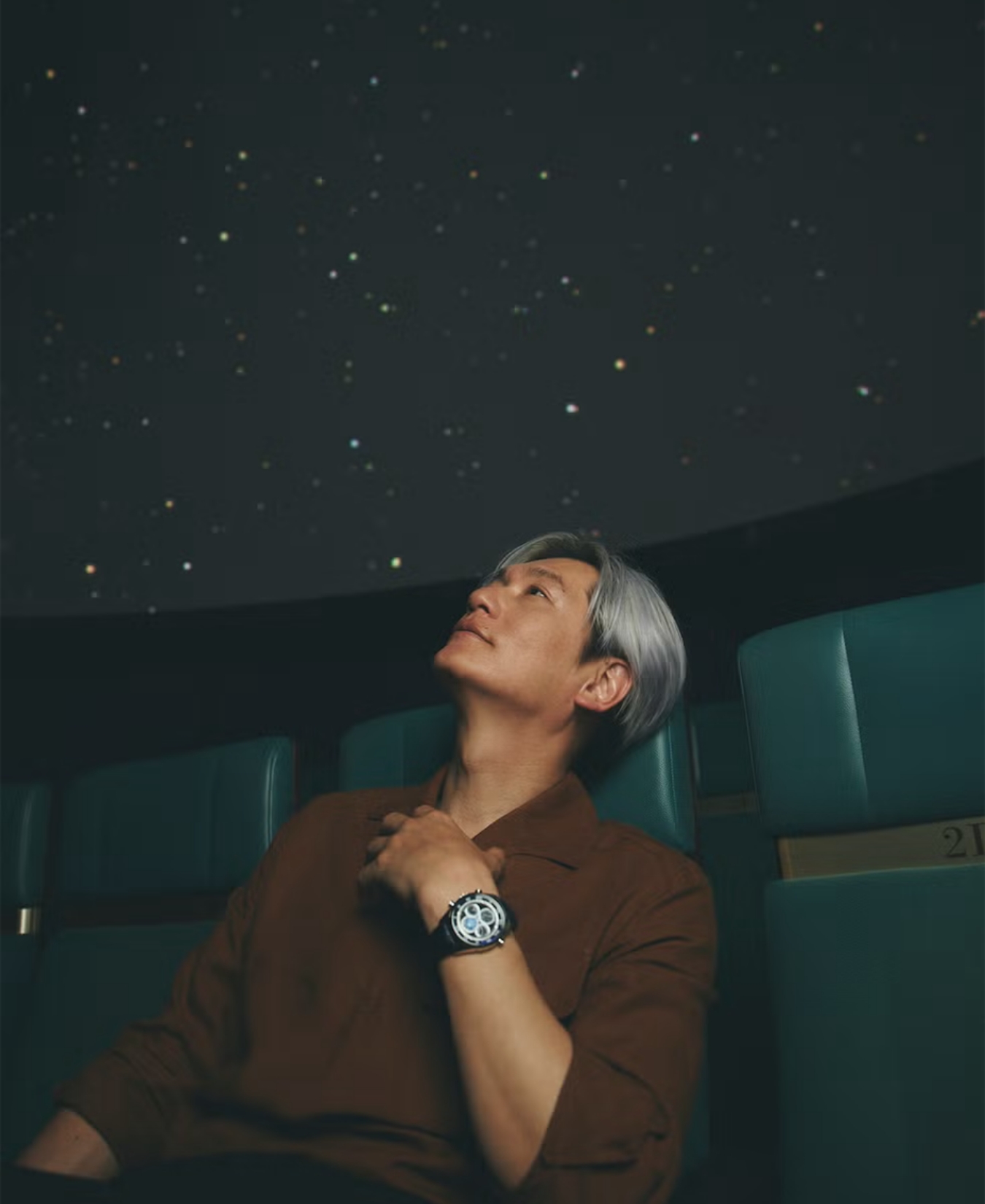 左腕に腕時計を身に着けた井浦新がプラネタリウムを見ている写真